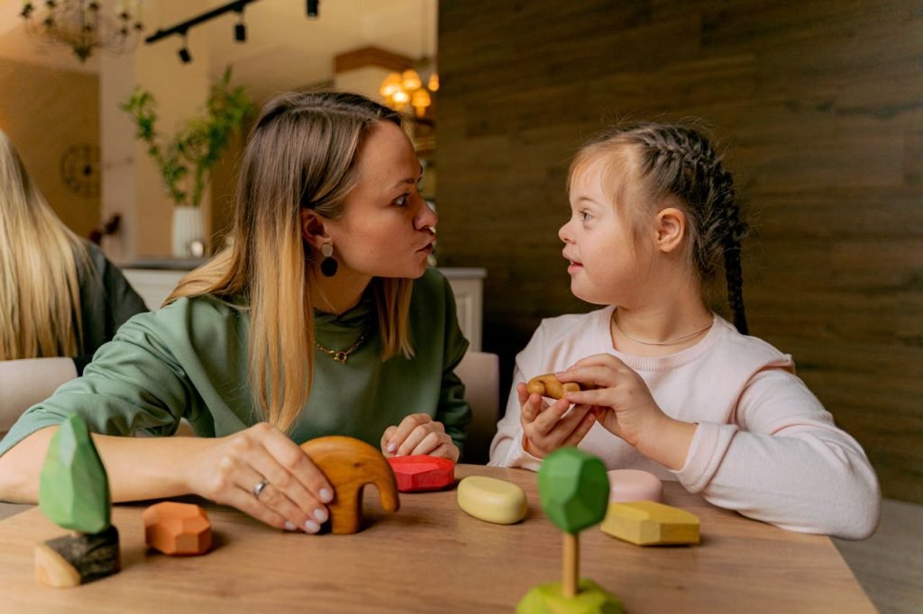 a-woman-and-girl-playing-together-6288088 An adult woman and a child with Down syndrome engaging in playful interaction with wooden toys indoors.